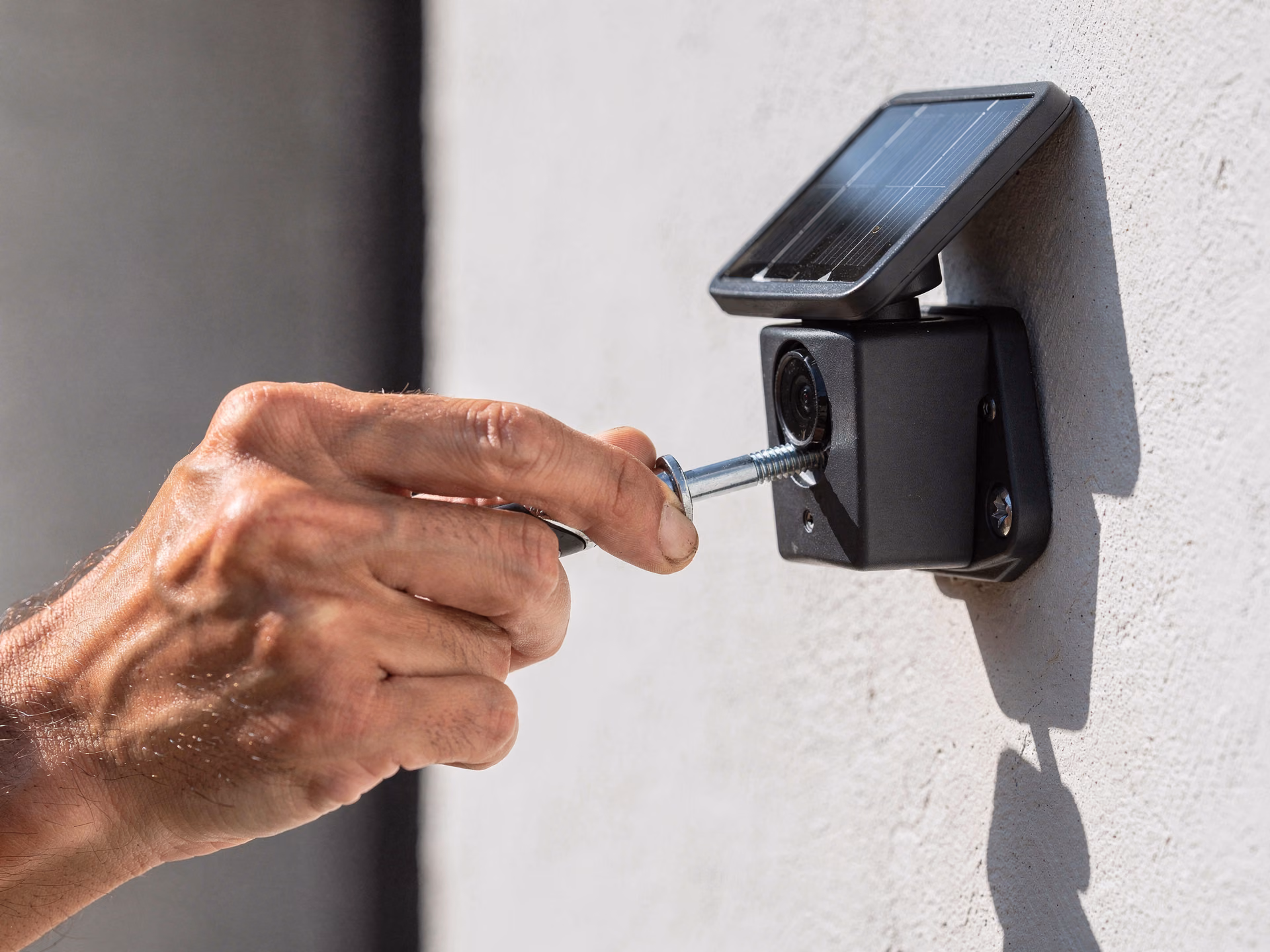 Détail d'une main fixant un support de caméra solaire sur un mur